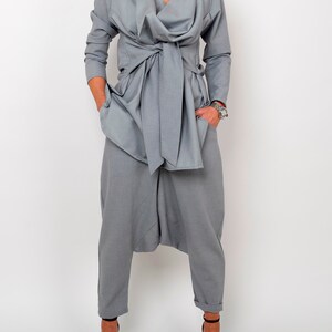 May include: A gray, long-sleeved top with a draped neckline and a tie at the waist. The top is paired with gray pants that have a loose, gathered fit.