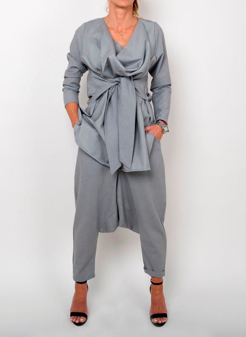 May include: A gray, long-sleeved top with a draped neckline and a tie at the waist. The top is paired with gray pants that have a loose, gathered fit.