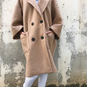 Może przedstawiać: Długi, dwurzędowy płaszcz w kolorze camel z dużymi kieszeniami na klapie. Płaszcz ma luźny kr&oacute;j i jest wykonany z miękkiej, puszystej tkaniny.