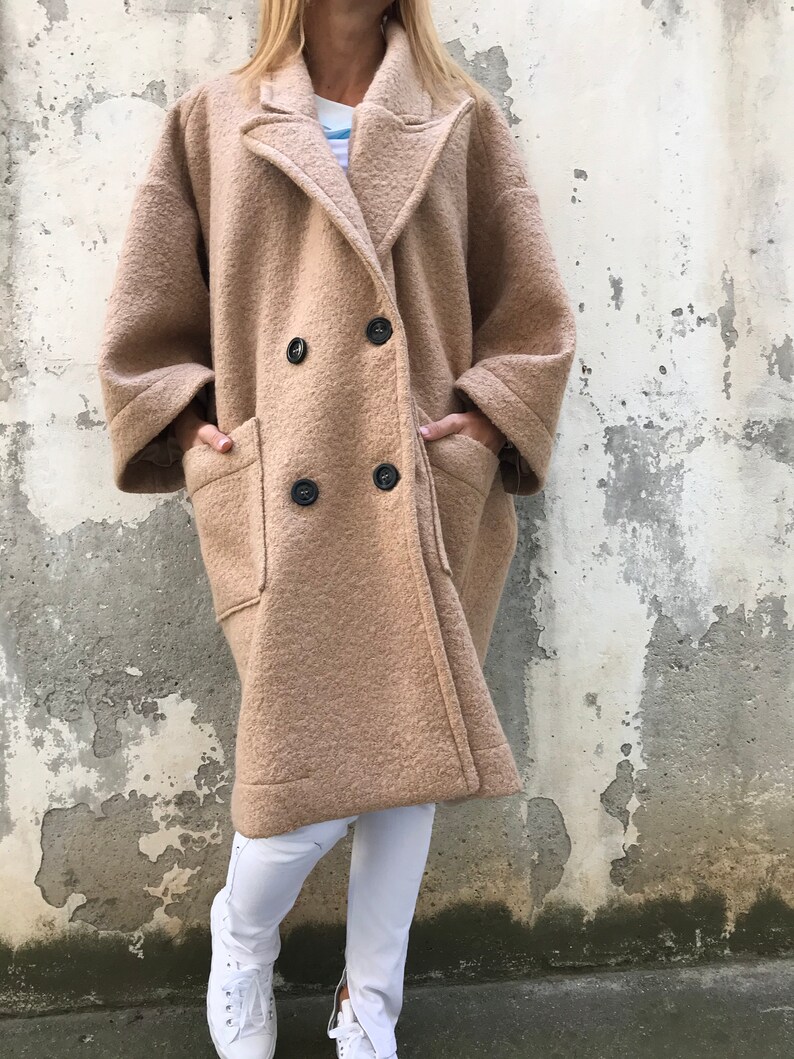 Może przedstawiać: Długi, dwurzędowy płaszcz w kolorze camel z dużymi kieszeniami na klapie. Płaszcz ma luźny kr&oacute;j i jest wykonany z miękkiej, puszystej tkaniny.