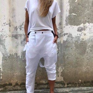 Puede incluir: Pantal&oacute;n blanco de lino con un dise&ntilde;o &uacute;nico que presenta un tiro bajo y un cierre de bot&oacute;n. El pantal&oacute;n es holgado y tiene un aspecto informal.