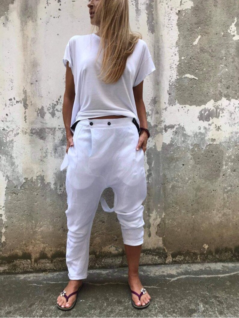 Puede incluir: Pantal&oacute;n blanco de lino con un dise&ntilde;o &uacute;nico que presenta un tiro bajo y un cierre de bot&oacute;n. El pantal&oacute;n es holgado y tiene un aspecto informal.