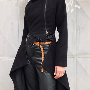 May include: A black asymmetrical jacket with a long, flowing back hem and a zipper closure. The jacket has a high collar and a belt.