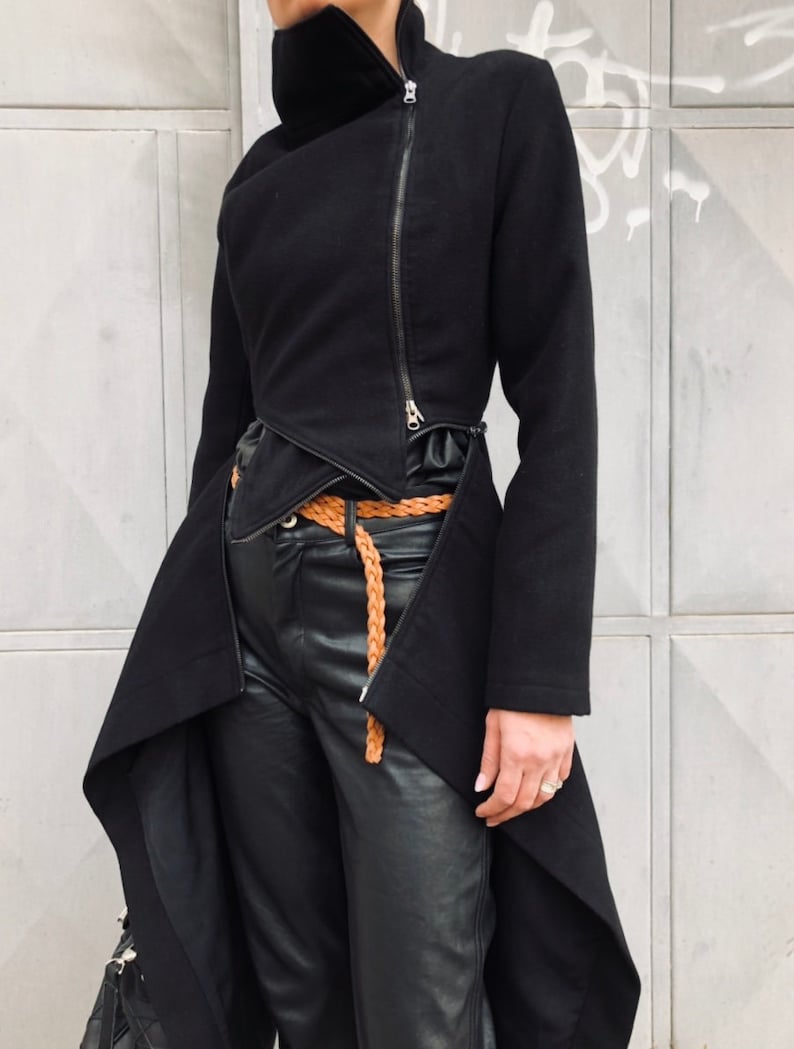 May include: A black asymmetrical jacket with a long, flowing back hem and a zipper closure. The jacket has a high collar and a belt.