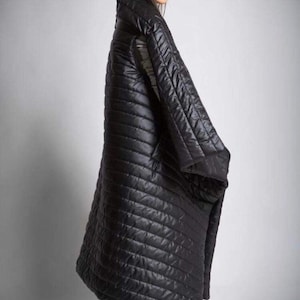 May include: A long, black quilted coat with a high collar. The coat has a diagonal stitched pattern and appears to be made of a shiny, water-resistant material. The coat is worn over gray pants and black shoes.
