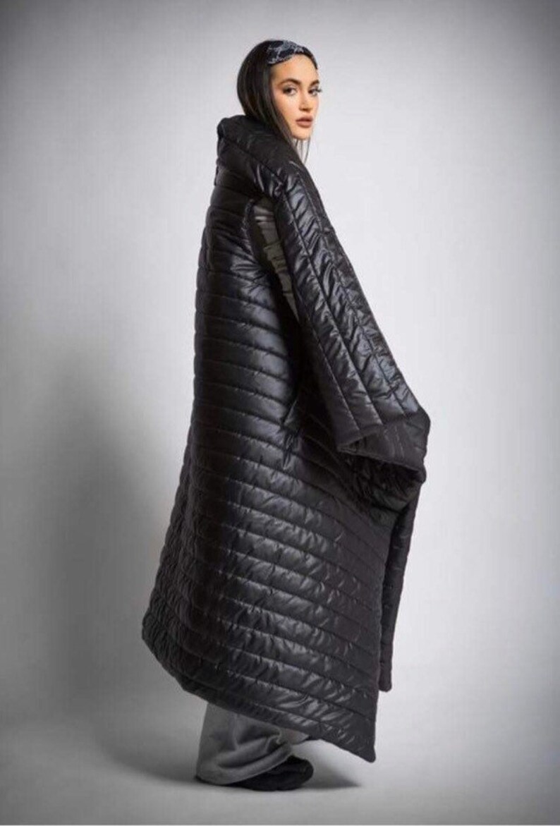May include: A long, black quilted coat with a high collar. The coat has a diagonal stitched pattern and appears to be made of a shiny, water-resistant material. The coat is worn over gray pants and black shoes.