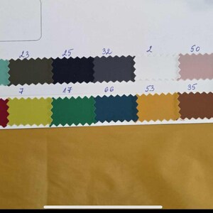 May include: A fabric swatch card with various color samples. The card includes a range of colors, from deep blue to pink, with a white background. The fabric is 155cm wide and made of 100% PL.