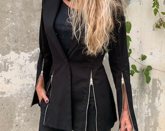 May include: A black blazer with long sleeves and multiple zips down the front and sides. The blazer has a fitted silhouette and a slightly flared hem.