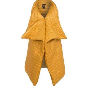 May include: Mustard yellow quilted scarf with a unique design. The scarf has a wide collar that tapers down into two long panels. The fabric has a subtle sheen and a diamond-shaped quilted pattern. The scarf is a fashion accessory.