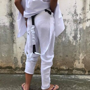 Puede incluir: Pantal&oacute;n blanco de lino con cintur&oacute;n y tirantes negros. El pantal&oacute;n tiene un corte holgado y fluido y est&aacute; remangado en los tobillos.