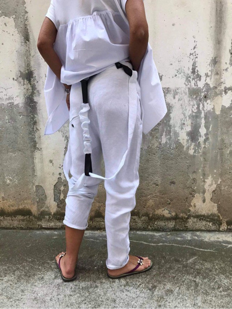 Puede incluir: Pantal&oacute;n blanco de lino con cintur&oacute;n y tirantes negros. El pantal&oacute;n tiene un corte holgado y fluido y est&aacute; remangado en los tobillos.