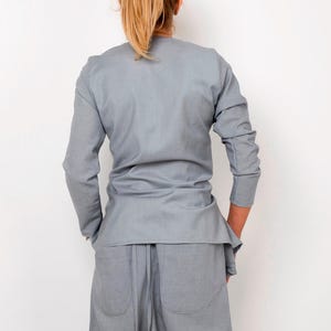 May include: A light gray long-sleeved shirt with a wrap-style design. The shirt is made of a soft, drapey fabric and has a relaxed fit.