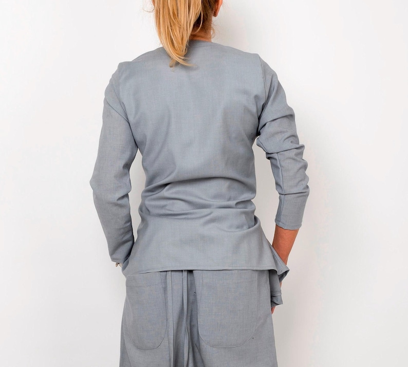 May include: A light gray long-sleeved shirt with a wrap-style design. The shirt is made of a soft, drapey fabric and has a relaxed fit.