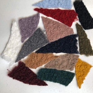 Może przedstawiać: Zestaw 14 pr&oacute;bek tkanin w r&oacute;żnych kolorach i fakturach. Pr&oacute;bki są wycięte w kształcie tr&oacute;jkąta i ułożone w p&oacute;łkole na białym tle.