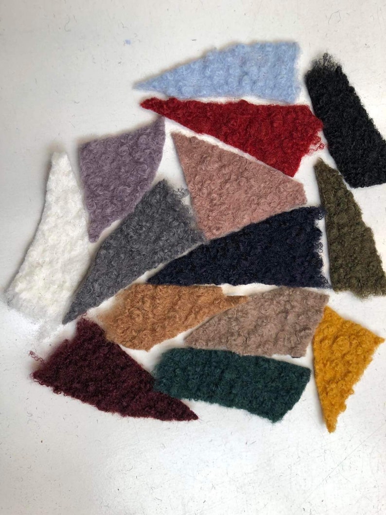 Może przedstawiać: Zestaw 14 pr&oacute;bek tkanin w r&oacute;żnych kolorach i fakturach. Pr&oacute;bki są wycięte w kształcie tr&oacute;jkąta i ułożone w p&oacute;łkole na białym tle.