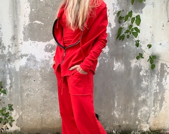 Op de afbeelding: Een rood hooded jack en bijpassende wijde broek. Het jack heeft een ritssluiting en een ontspannen pasvorm. De broek heeft een trekkoord in de taille en zakken.
