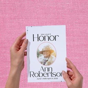 Può includere: Una scheda commemorativa con le parole "We Love & Honor". Presenta una foto di una donna con un cappello, il nome "Ann Robertson" e le date "June 1, 1949-April 21, 2026". Lo sfondo è rosa.