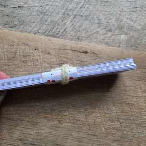 Puede incluir: Una pila de tarjetas blancas en blanco con un papel estampado de lunares rosa y rojo envuelto alrededor del medio y atado con una cuerda.