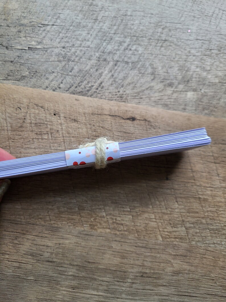 Puede incluir: Una pila de tarjetas blancas en blanco con un papel estampado de lunares rosa y rojo envuelto alrededor del medio y atado con una cuerda.