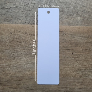 Puede incluir: Un marcador de libros en blanco, de color azul claro, con un agujero en la parte superior. El marcador mide 17,8 cm de alto y 5,1 cm de ancho.