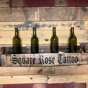 Pu&ograve; includere: Un porta bottiglie in legno realizzato con una botte riciclata con un accento in metallo nero. Il porta bottiglie &egrave; montato su una parete e ha quattro bottiglie di vino. Il porta bottiglie &egrave; etichettato "Square Rose Tattoo".