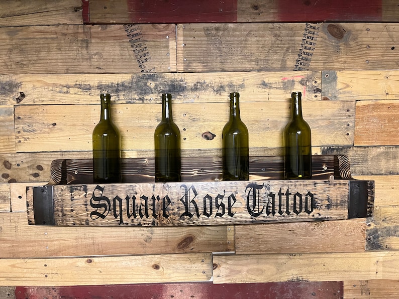 Pu&ograve; includere: Un porta bottiglie in legno realizzato con una botte riciclata con un accento in metallo nero. Il porta bottiglie &egrave; montato su una parete e ha quattro bottiglie di vino. Il porta bottiglie &egrave; etichettato "Square Rose Tattoo".
