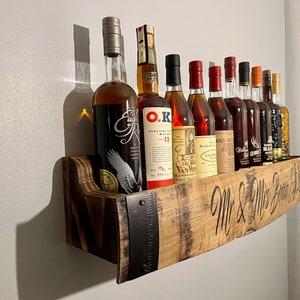 Pu&ograve; includere: Uno scaffale in legno realizzato con un barile riciclato con accenti in metallo, che contiene una collezione di bottiglie di liquore. Lo scaffale &egrave; inciso con il testo "Mr. & Mrs. Better Half".