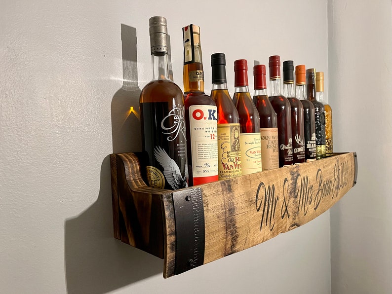 Pu&ograve; includere: Uno scaffale in legno realizzato con un barile riciclato con accenti in metallo, che contiene una collezione di bottiglie di liquore. Lo scaffale &egrave; inciso con il testo "Mr. & Mrs. Better Half".