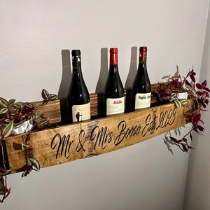 Pu&ograve; includere: Un porta bottiglie in legno con l'iscrizione "Mr & Mrs Bosso Est 2022" e tre bottiglie di vino. Il porta bottiglie &egrave; decorato con del verde.