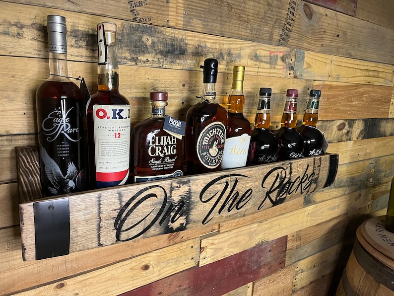 Pu&ograve; includere: Uno scaffale in legno con le parole "On The Rocks" intagliate su di esso. Lo scaffale contiene sette bottiglie di liquore, tra cui Eagle Rare, O.K.I., Elijah Craig e Michters. Lo scaffale &egrave; montato su una parete in legno.