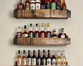 May include: Three rustic wooden shelves, each holding multiple bottles of liquor. The shelves are made from reclaimed wood and have metal accents. The bottles vary in size and shape, with a variety of labels. The text "Complimentary Custom Sizing" is at the bottom.