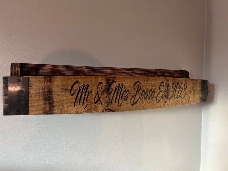 Pu&ograve; includere: Un ripiano in legno realizzato con una botte di vino riciclata con accenti in metallo. Il ripiano &egrave; inciso con il testo "Mr & Mrs Bosso Est 2023".