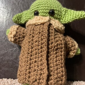 Peut inclure: Un jouet en peluche vert et marron crochet&eacute; ressemblant &agrave; un personnage de la franchise Star Wars. Le jouet porte un manteau marron avec un col beige.