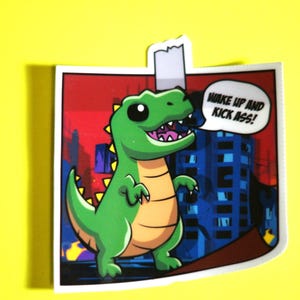 May include: A sticker featuring a cartoon green dinosaur with yellow accents, standing in front of a city skyline. The dinosaur has a speech bubble that says "WAKE UP AND KICK ASS!". The sticker is on a yellow background.