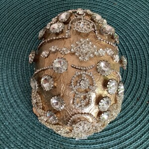 May include: A gold-colored egg-shaped object covered in rhinestones and glitter.