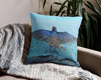 Puede incluir: Cojín cuadrado con un diseño de pájaro azul y turquesa. El pájaro está representado con las alas extendidas, en un estilo de pintura de acuarela. El cojín está colocado sobre una manta estampada.