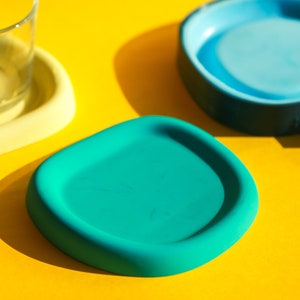 May include: Three colourful coasters, one yellow, one teal and one blue. The coasters are made of a soft, flexible material and are perfect for protecting surfaces from spills and scratches.