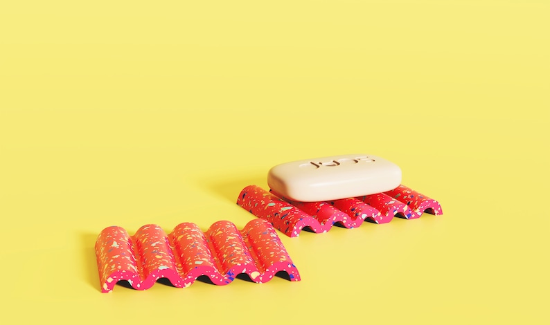 Puede incluir: Dos jaboneras onduladas con manchas de color rosa y blanco. Una jabonera tiene una pastilla de jab&oacute;n blanca encima.