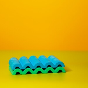 Puede incluir: Una pila de dos bloques de construcci&oacute;n de pl&aacute;stico ondulados, azul y verde, sobre una superficie amarilla.