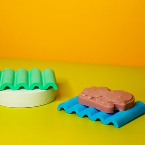 Puede incluir: Dos plataformas onduladas, una verde y una azul, con una pastilla de jab&oacute;n marr&oacute;n encima de la plataforma azul. Las plataformas est&aacute;n sobre una superficie amarilla.