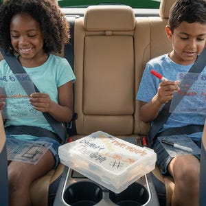 Peut inclure: Deux enfants dans une voiture sont assis et tiennent des feuilles de plastique transparentes avec du texte et un motif quadrill&eacute;. Un r&eacute;cipient en plastique transparent avec divers articles est plac&eacute; entre eux. Les enfants sourient et semblent utiliser les feuilles avec des marqueurs.