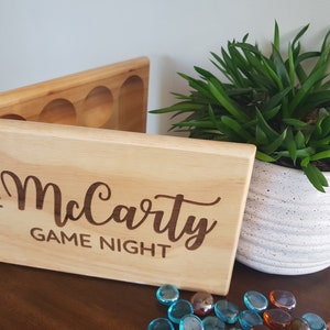 May include: A wooden box with a hinged lid and compartments for game pieces. The box is engraved with the text "The McCarty Game Night".