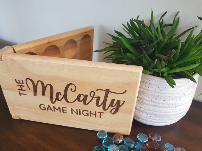 May include: A wooden box with a hinged lid and compartments for game pieces. The box is engraved with the text "The McCarty Game Night".
