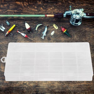 May include: A clear plastic tackle box with multiple compartments for storing fishing lures. The box is empty and sitting on a wooden surface. There are various fishing lures scattered around the box, including a red and white lure, a green and white lure, and a silver lure.