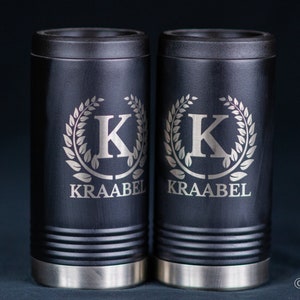 May include: Two black insulated can coolers with silver bases. Each cooler features a silver engraved wreath with the letter "K" in the center and the text "KRAABEL" below.