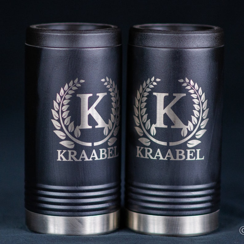 May include: Two black insulated can coolers with silver bases. Each cooler features a silver engraved wreath with the letter "K" in the center and the text "KRAABEL" below.