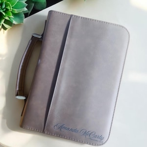 May include: A brown faux leather bible cover with a silver handle and the name "Amanda McCarty" and the text "Proverbs 3:5-6" embossed in blue.