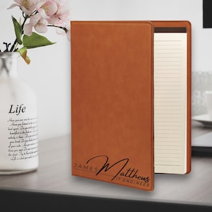 May include: A brown leatherette journal with a notepad insert. The journal has the name "JAMES Matthews IT ENGINEER" engraved on the front.