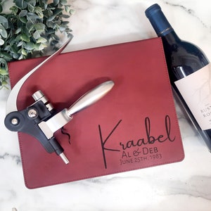 May include: A red leatherette wine bottle stopper holder with a silver and black corkscrew. The holder is engraved with the text "Kraabel AL & DEB JUNE 25TH, 1983".