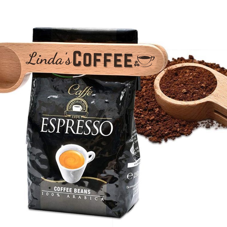 May include: A wooden coffee scoop with the text "Linda's COFFEE" and a small coffee cup icon. The scoop is holding a bag of espresso coffee beans. The bag is black with white text that says "Caffe Espresso 1895 Coffee Beans 100% Arabica".